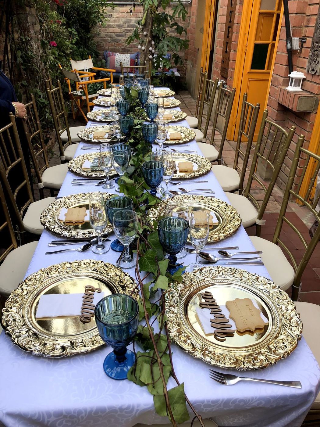Mesa larga en la terraza con platos dorados y copas azules