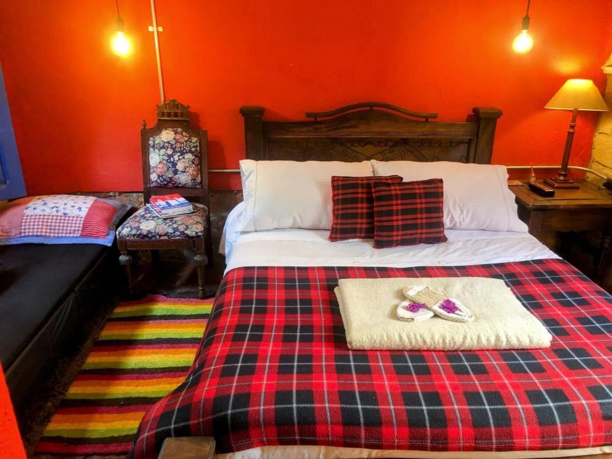 Habitación La Campesina: cama de cabecera tallada con manta escocesa roja y pared roja