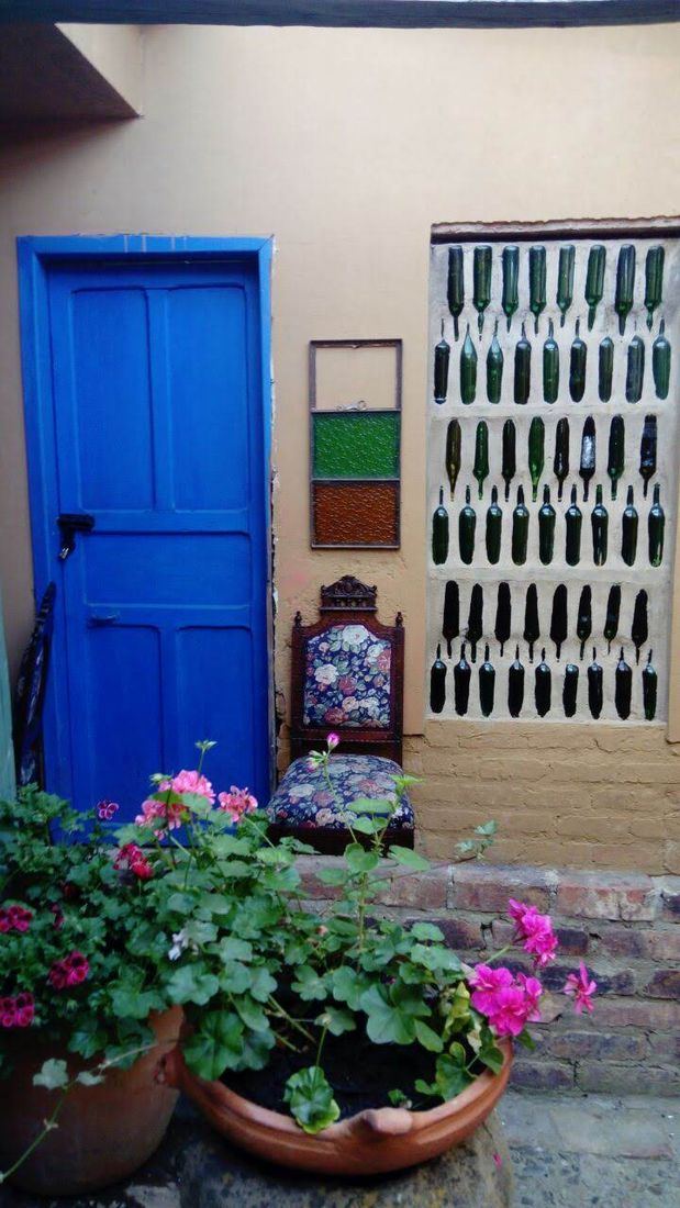 Puerta azul, geranios y muro de botellas